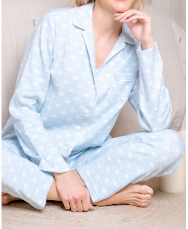 Una mujer cómoda sentada en el suelo viste pijama camisero de invierno azul vigoré estampado topos.