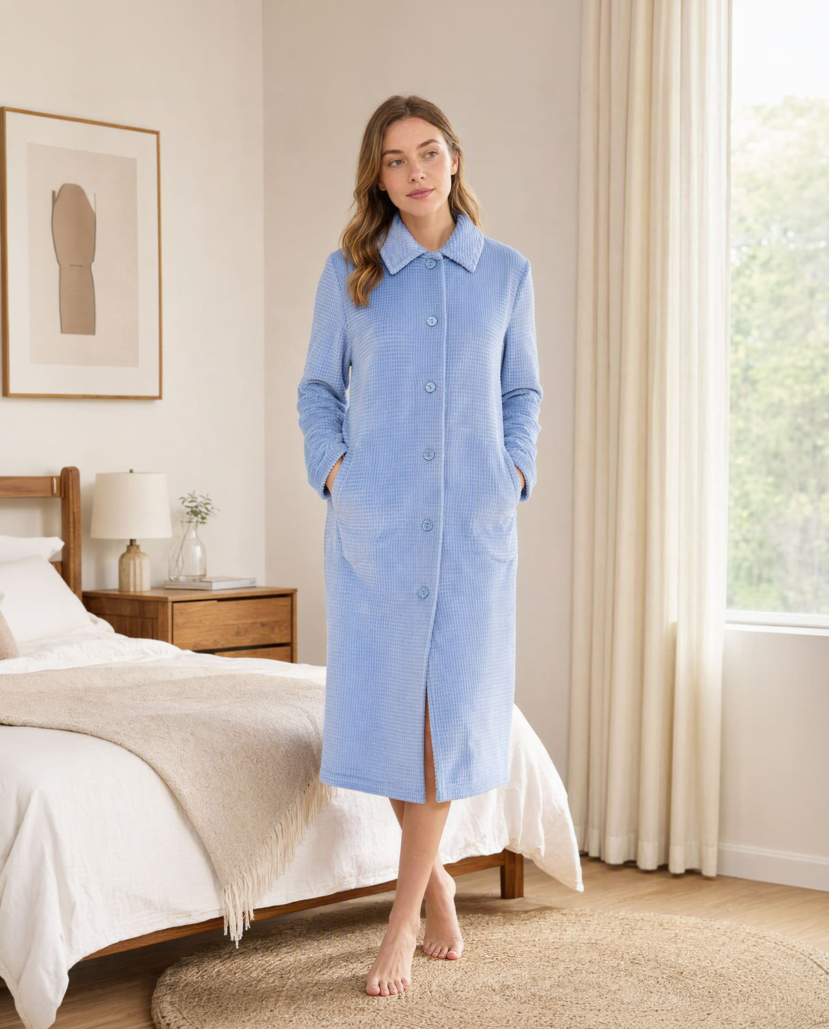 Mujer en un dormitorio con una bata larga azul de Lohe, modelo abotonado con diseño jacquard de cuadros en color acero.