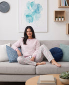 Mujer sentada en un sofá con el pijama de invierno Lohe de manga larga, confeccionado en borreguillo de color malva y pantalones a cuadros.