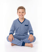 Niño sonriente sentado vestido con pijama de color azul con estampado de perritos y ribetes en azul oscuro