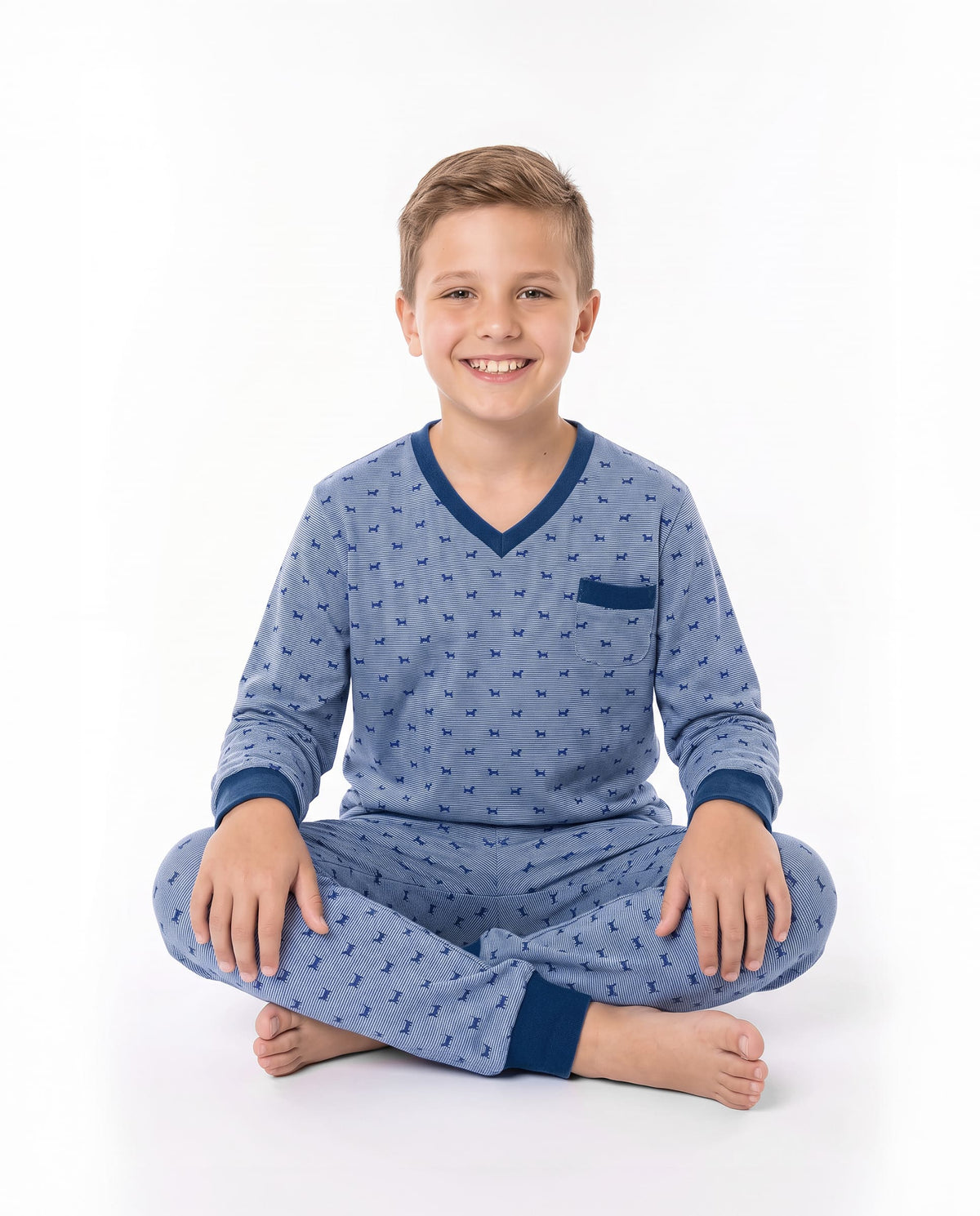 Niño sonriente sentado vestido con pijama de color azul con estampado de perritos y ribetes en azul oscuro