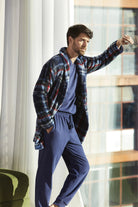 Hombre con bata de cuadros azules y pijama a juego junto a una ventana