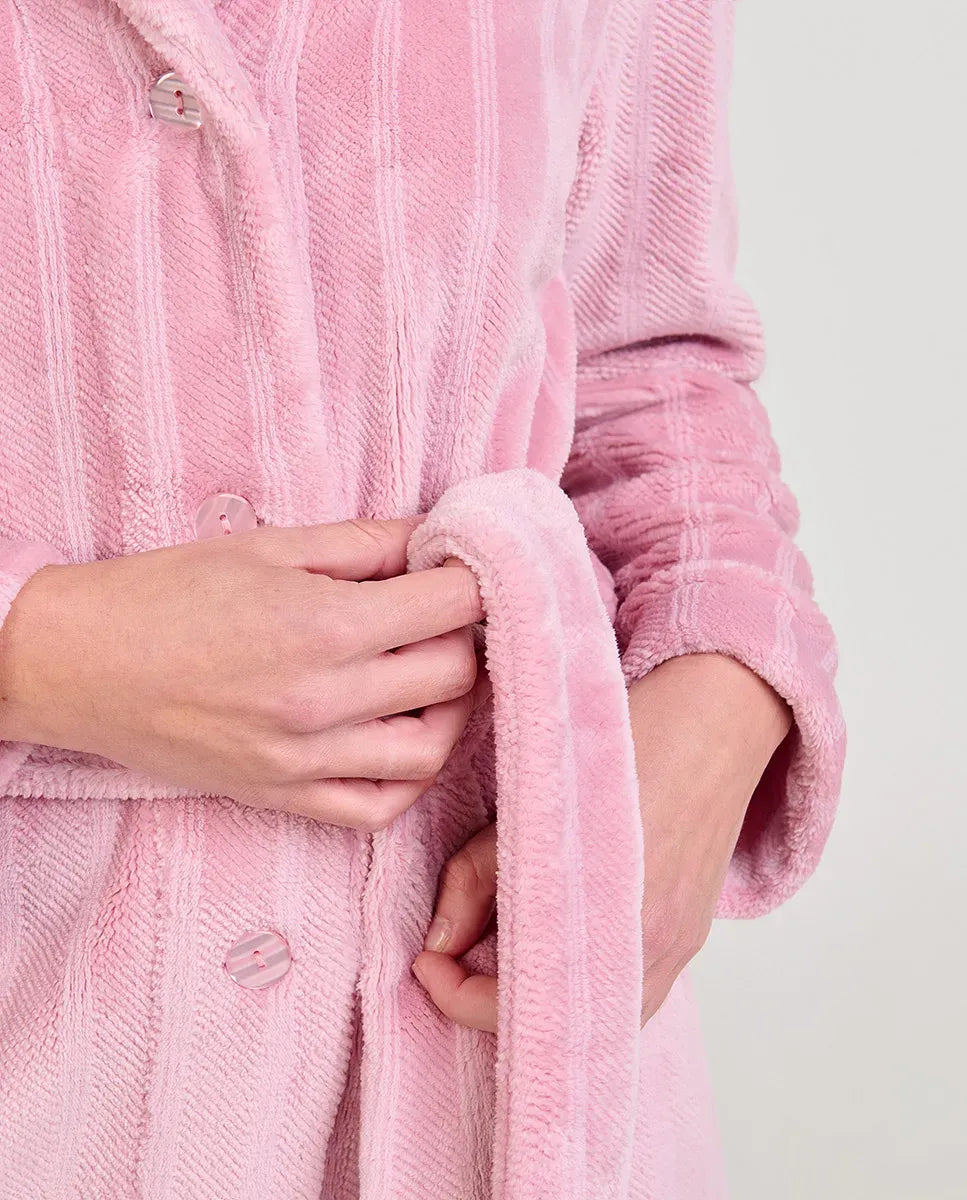 Mujer en camisón rosa claro y una bata Jacquard rosa a juego sentada en una mesa de madera junto a una ventana