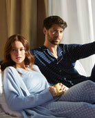 Pareja en pijama sentada sobre la cama, momento relajado en casa.