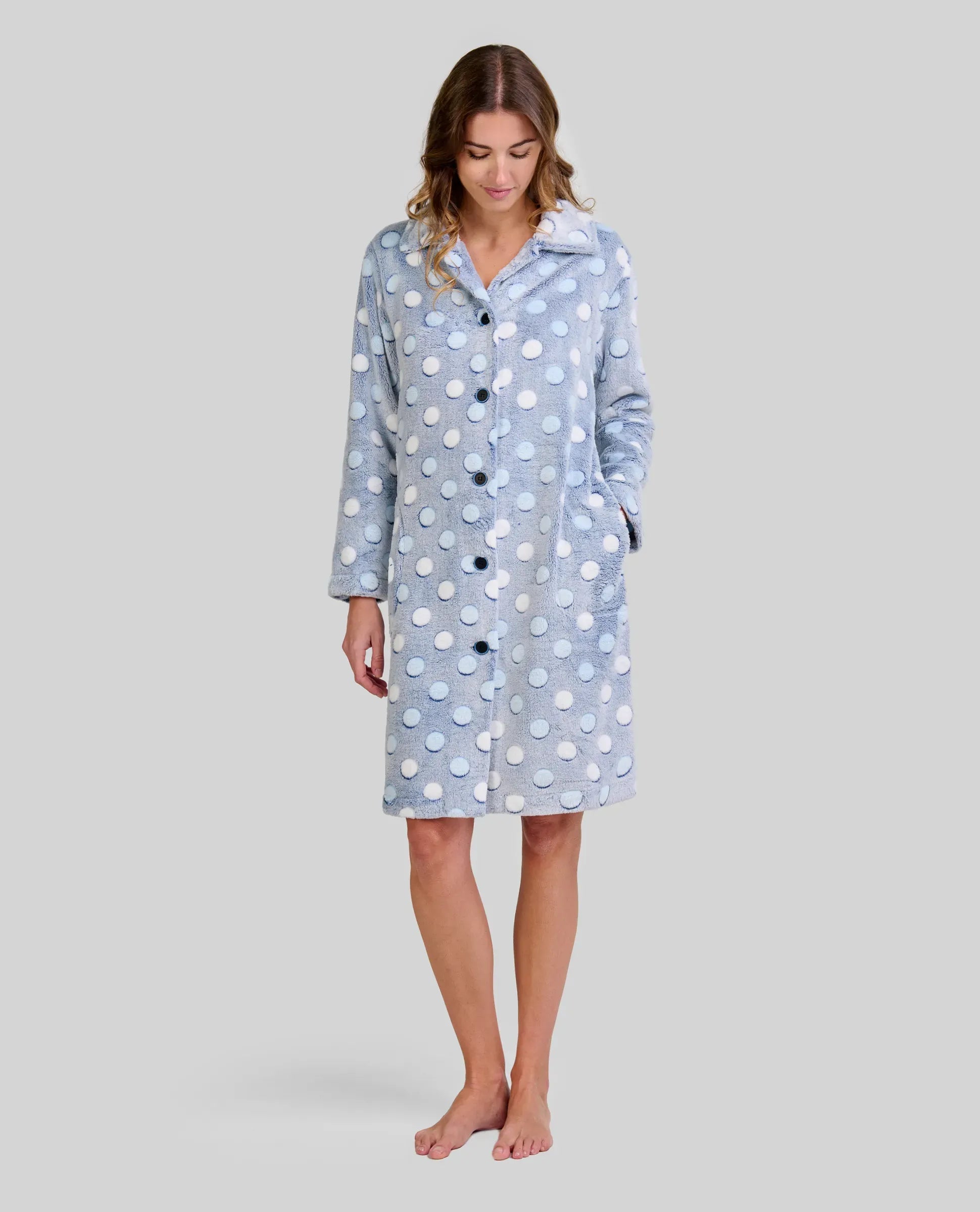 Mujer en bata celeste de lunares en relieve hasta la rodilla, manga larga y botones con bolsillos laterales.