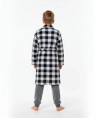 Niño de espaldas con cómoda bata a cuadros blanco y negro sobre pijama gris de terciopelo para invierno