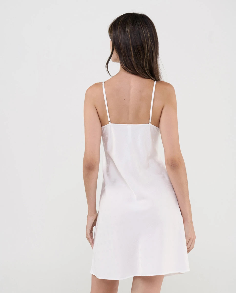 Vista de espaldas de mujer con sensual camisón corto de tirantes color marfil