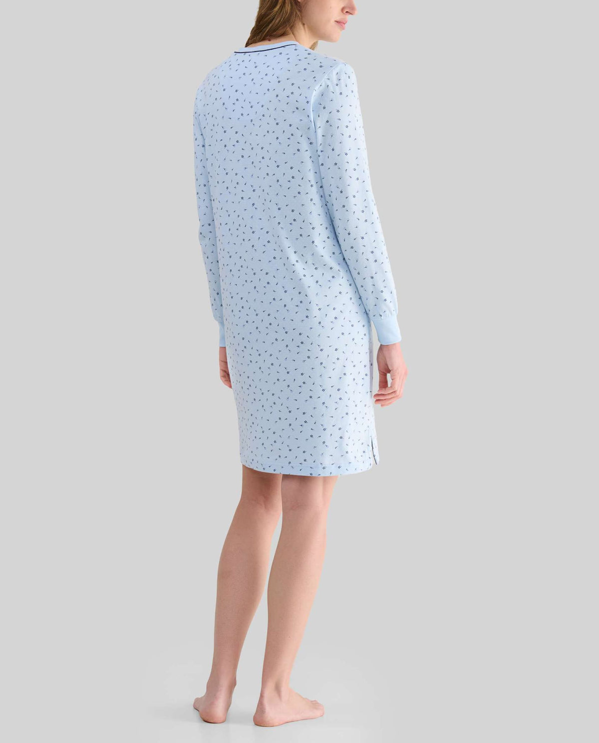 Mujer con top lencero celeste de manga larga, detalles de encaje blanco, botones, bolsillo en el pecho y lazo blanco decorativo.