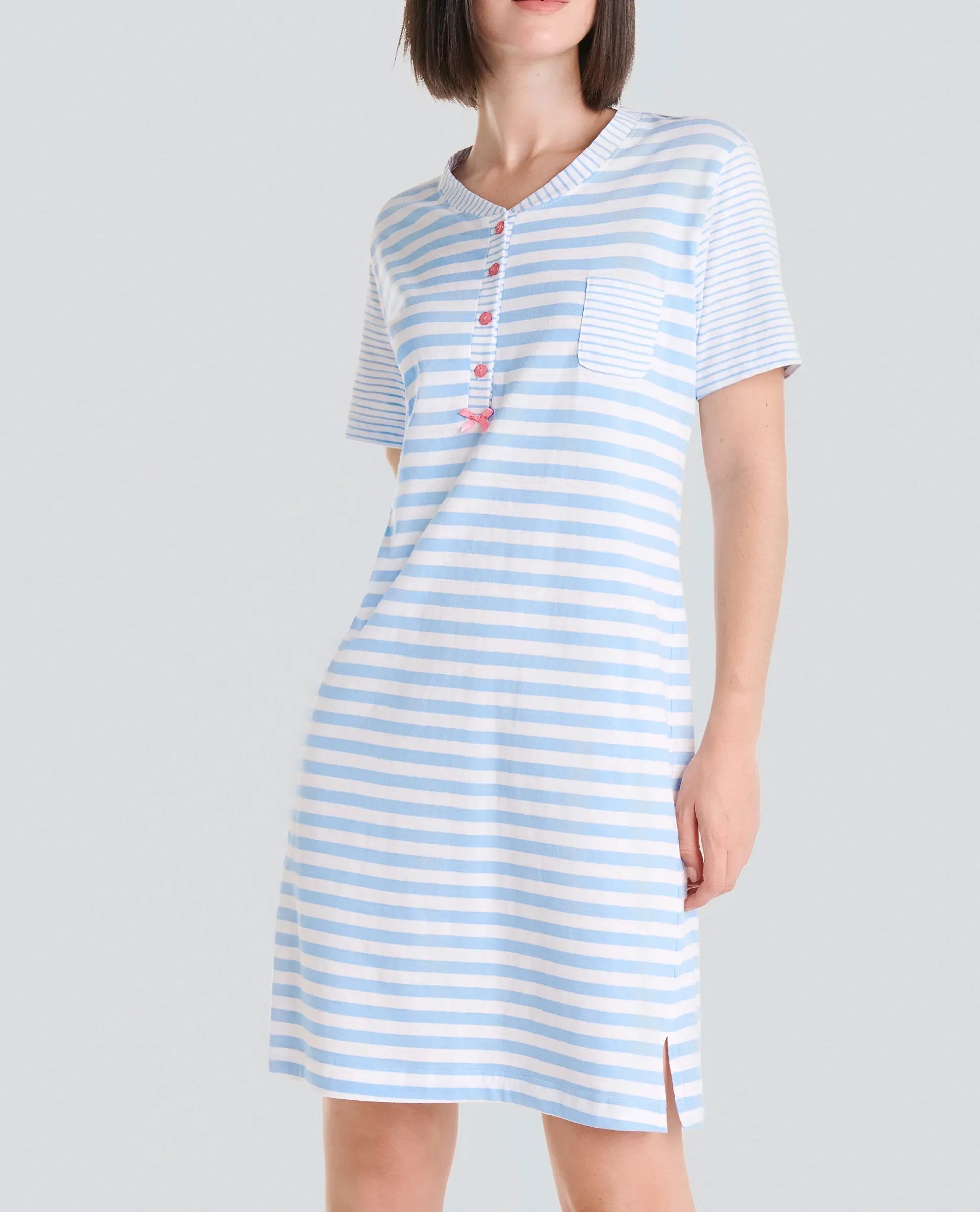 Mujer con camisón rosa claro de manga corta y hasta la rodilla, estampado floral blanco, ribete blanco y botones en el cuello.