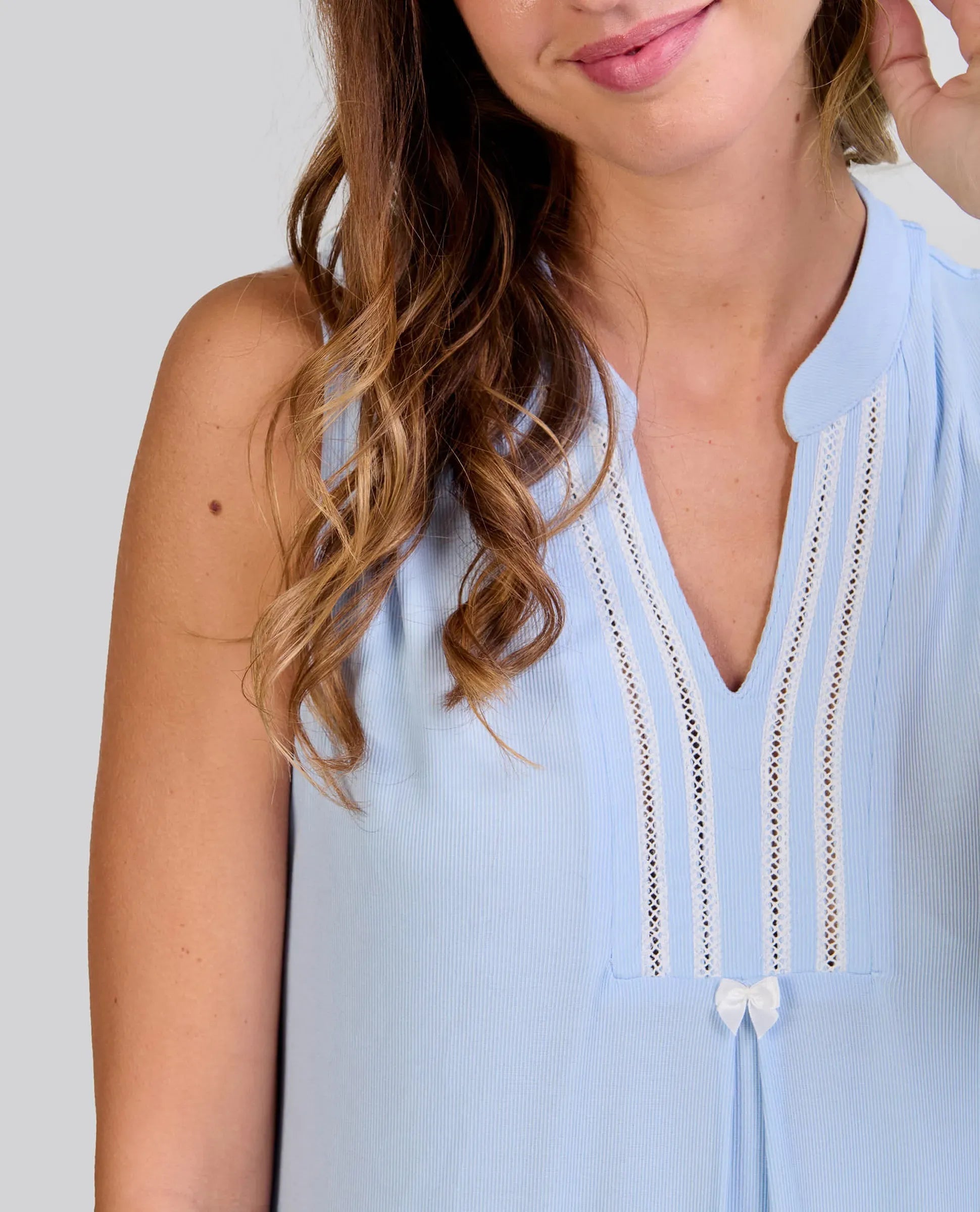 Detalle de camisón lencero sin mangas rosa claro con escote adornado con encaje y un pequeño lazo