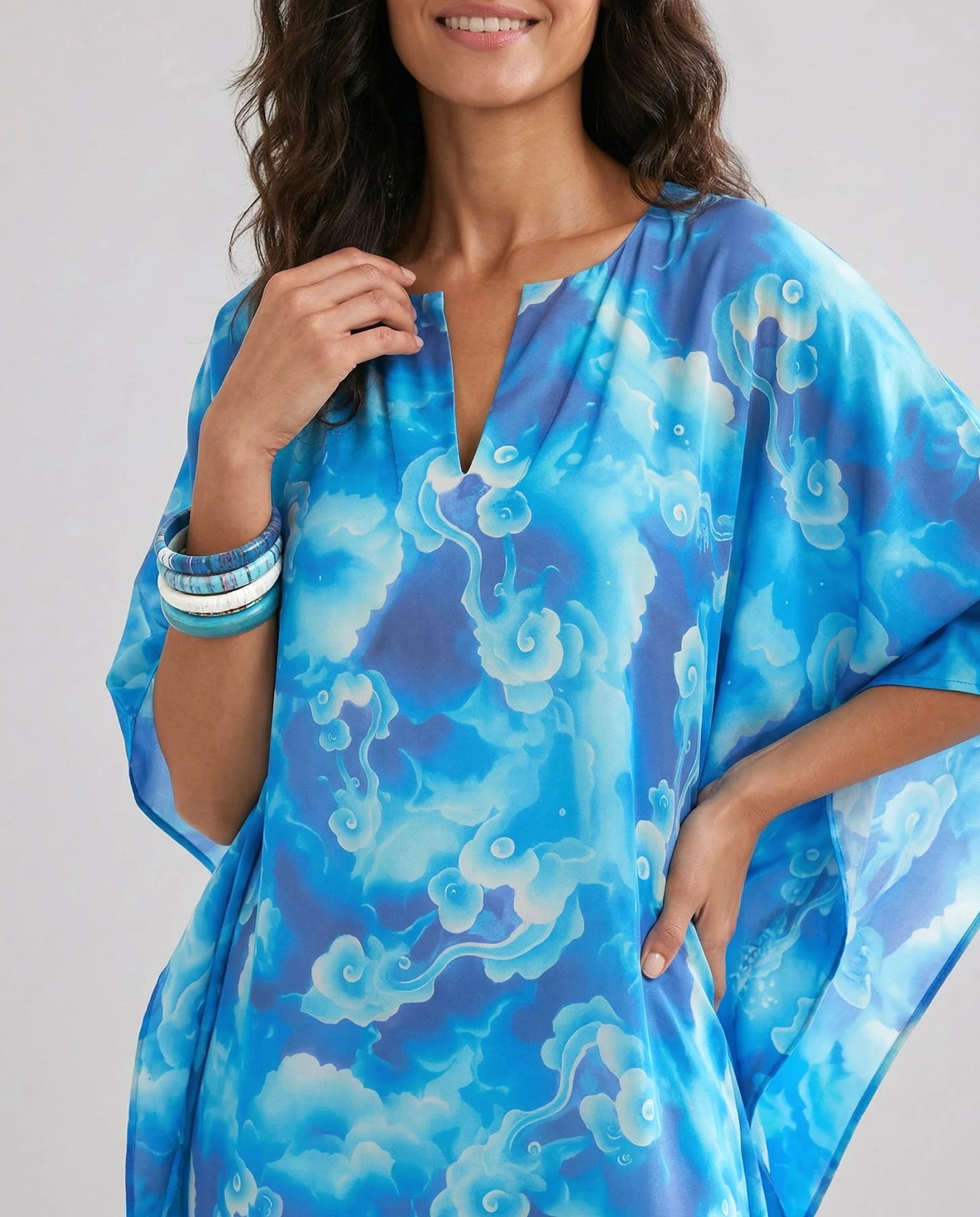 Vista detalle de mujer con kaftan azul de estampado abstracto, con pulseras en la muñeca.