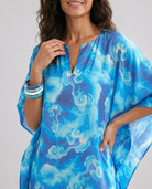 Vista detalle de mujer con kaftan azul de estampado abstracto, con pulseras en la muñeca.