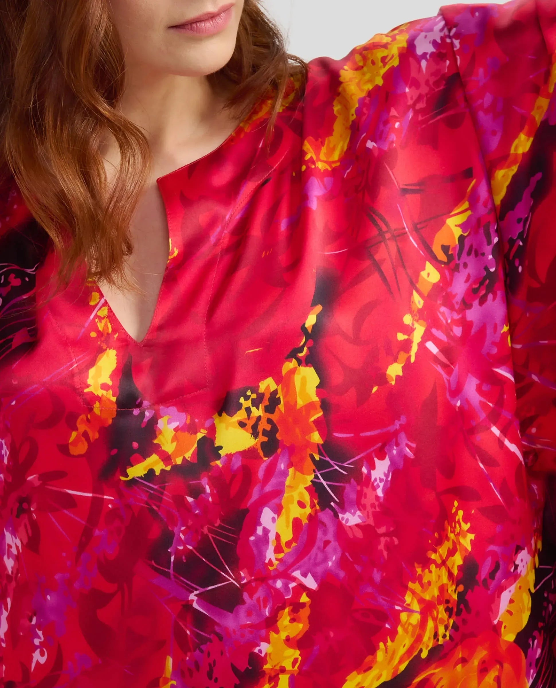 Mujer luciendo caftán de seda de color rojo con un llamativo estampado floral y detalles en amarillo y negro.