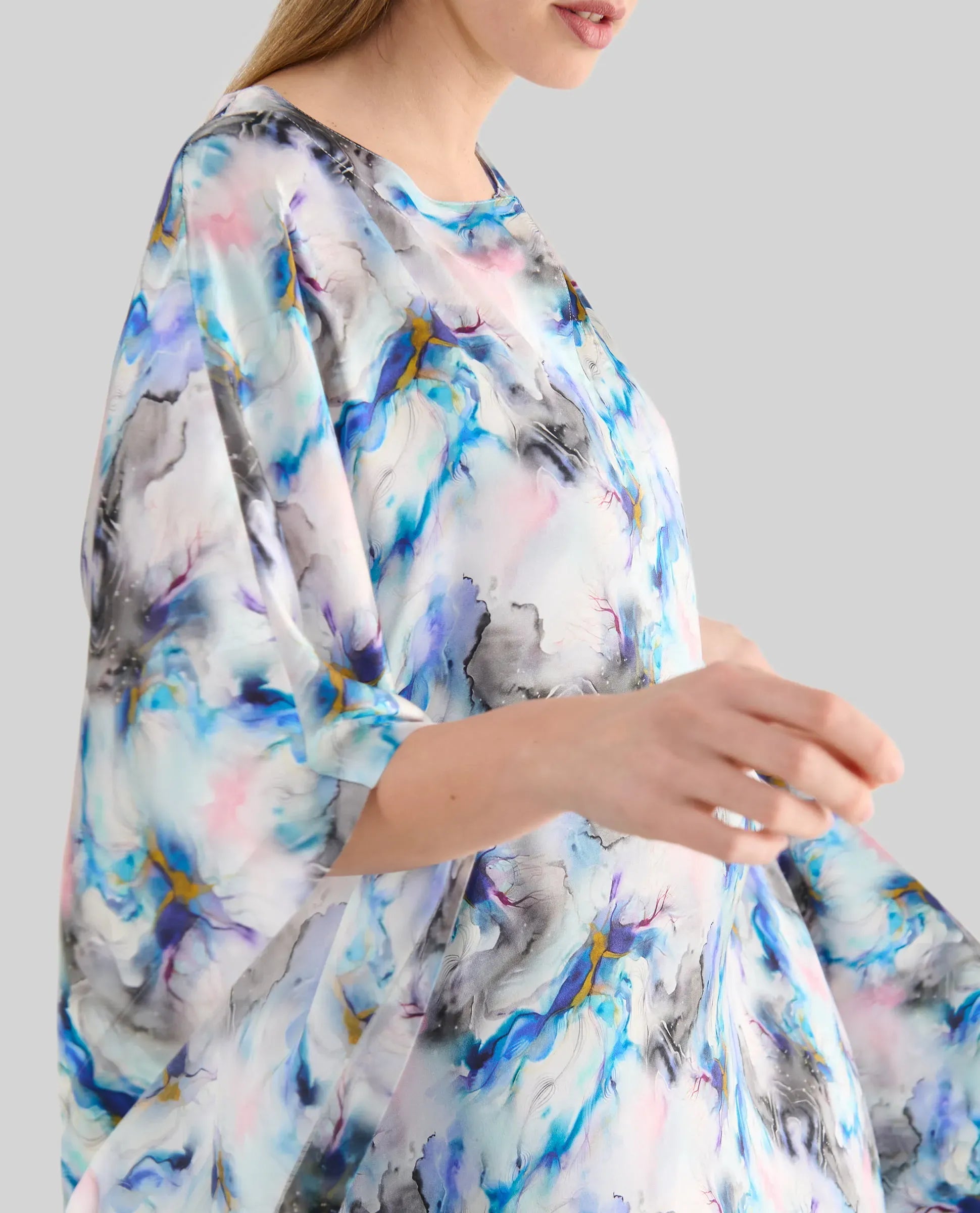 detalle de mujer luciendo un caftán fluido de estampado abstracto en tonalidades azul, rosa y gris con manga al codo