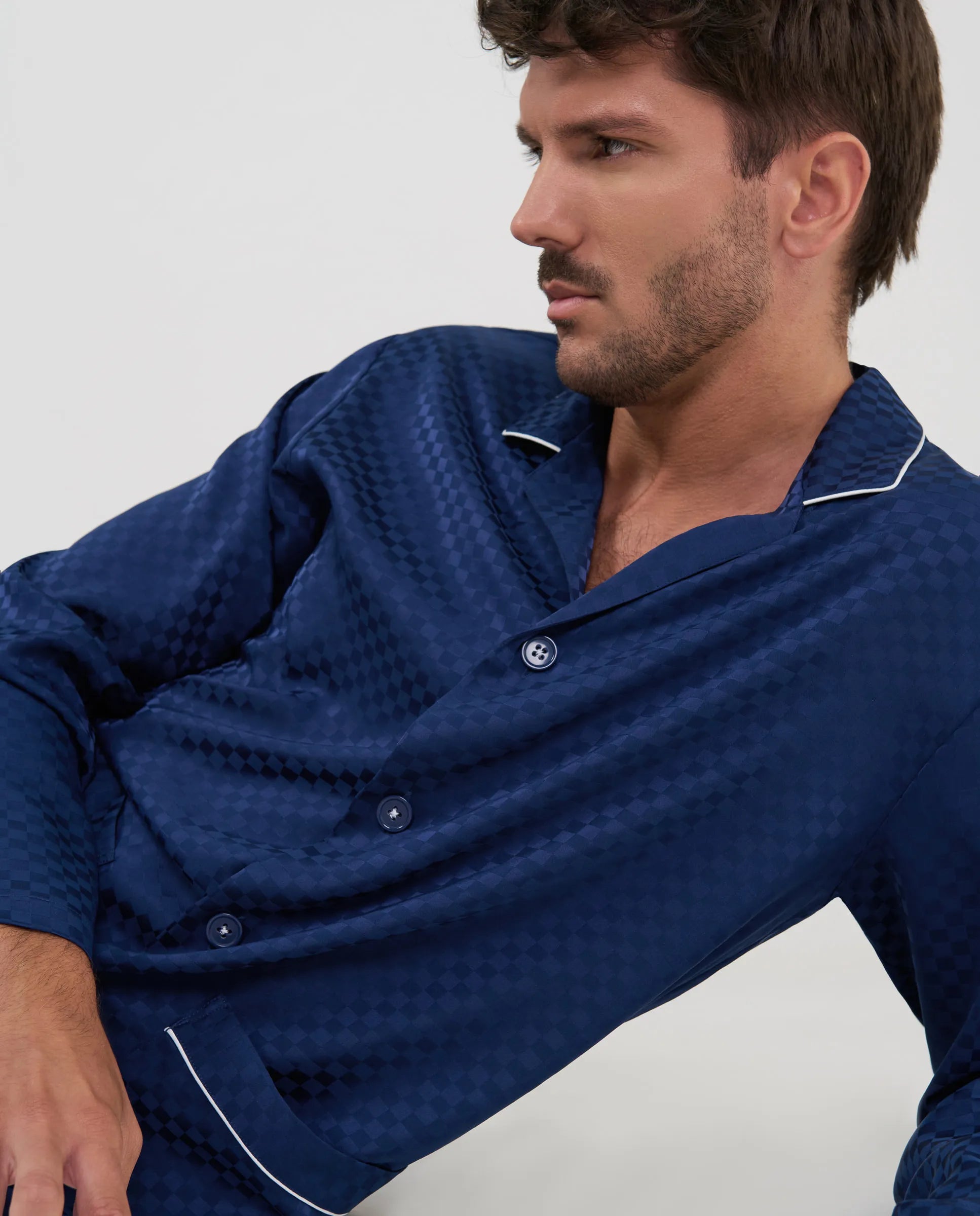 Primer plano del tejido jacquard con patrón de cuadros marino y detalle de botones en el pijama de hombre.