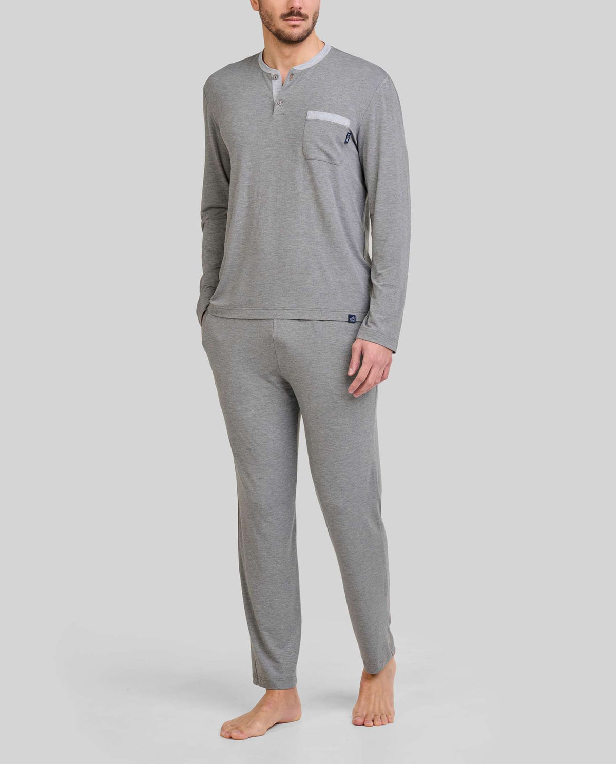Hombre luce pijama modal gris, cuello abotonado, mangas y pantalones largos, cintura ajustable y bolsillos laterales.