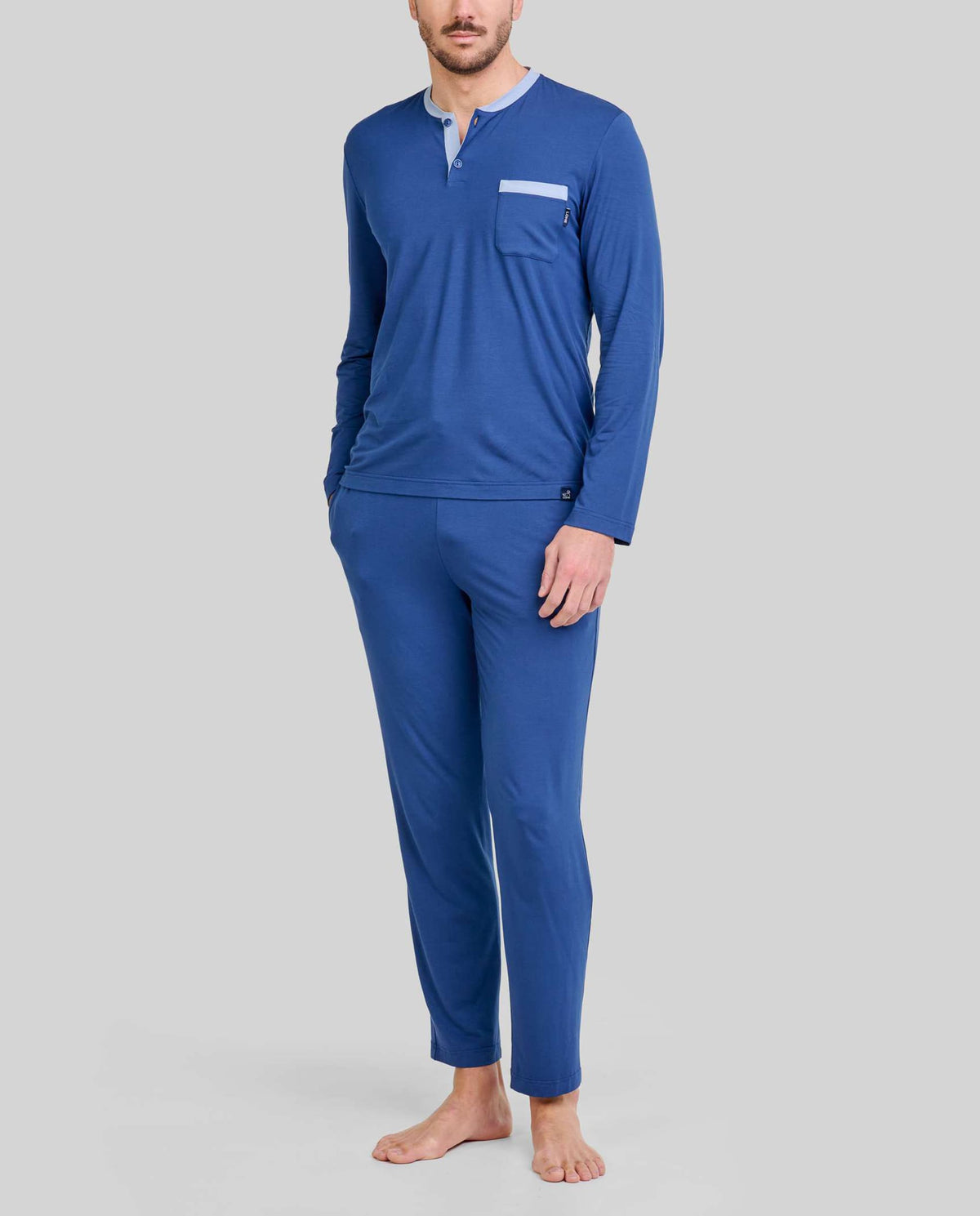 Hombre viste pijama modal azul marino de cuello abotonado, mangas y pantalones largos, cintura ajustable y bolsillos laterales.