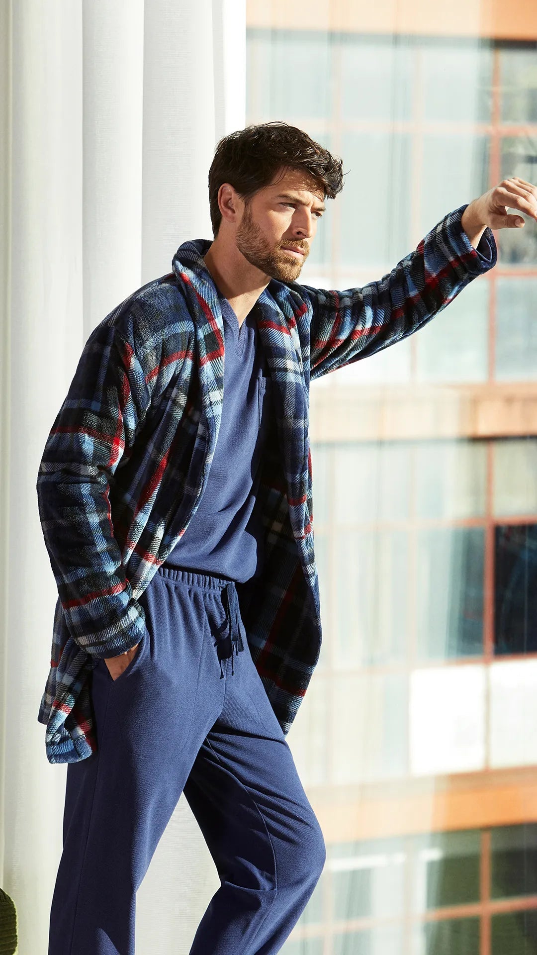 Hombre con bata y pijama de cuadros azules junto a una ventana