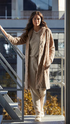 Mujer lleva bata beige texturizada y conjunto de pijama canale camel y pantuflas