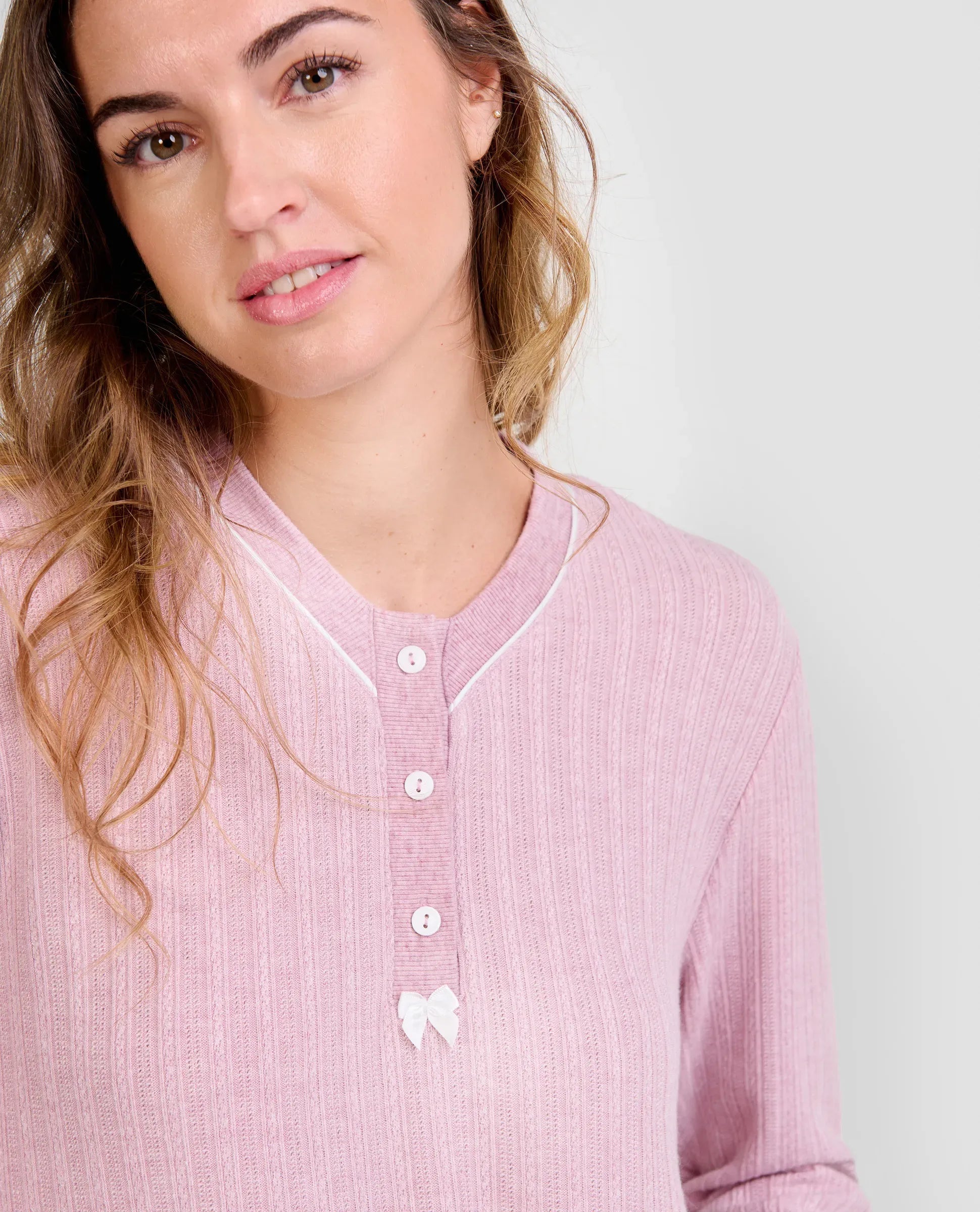 Mujer luce chaquetilla de pijama de invierno rosa de manga larga, cuello con botones blancos y lazo