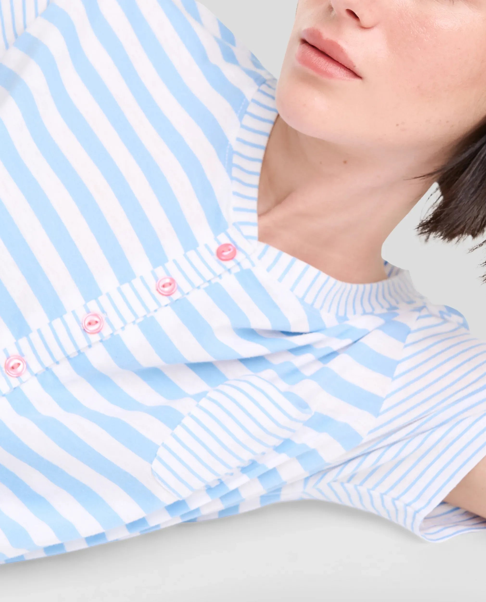 Vista detalle de mujer con camiseta de manga corta a rayas para dormir este verano y cuello con botones rosas