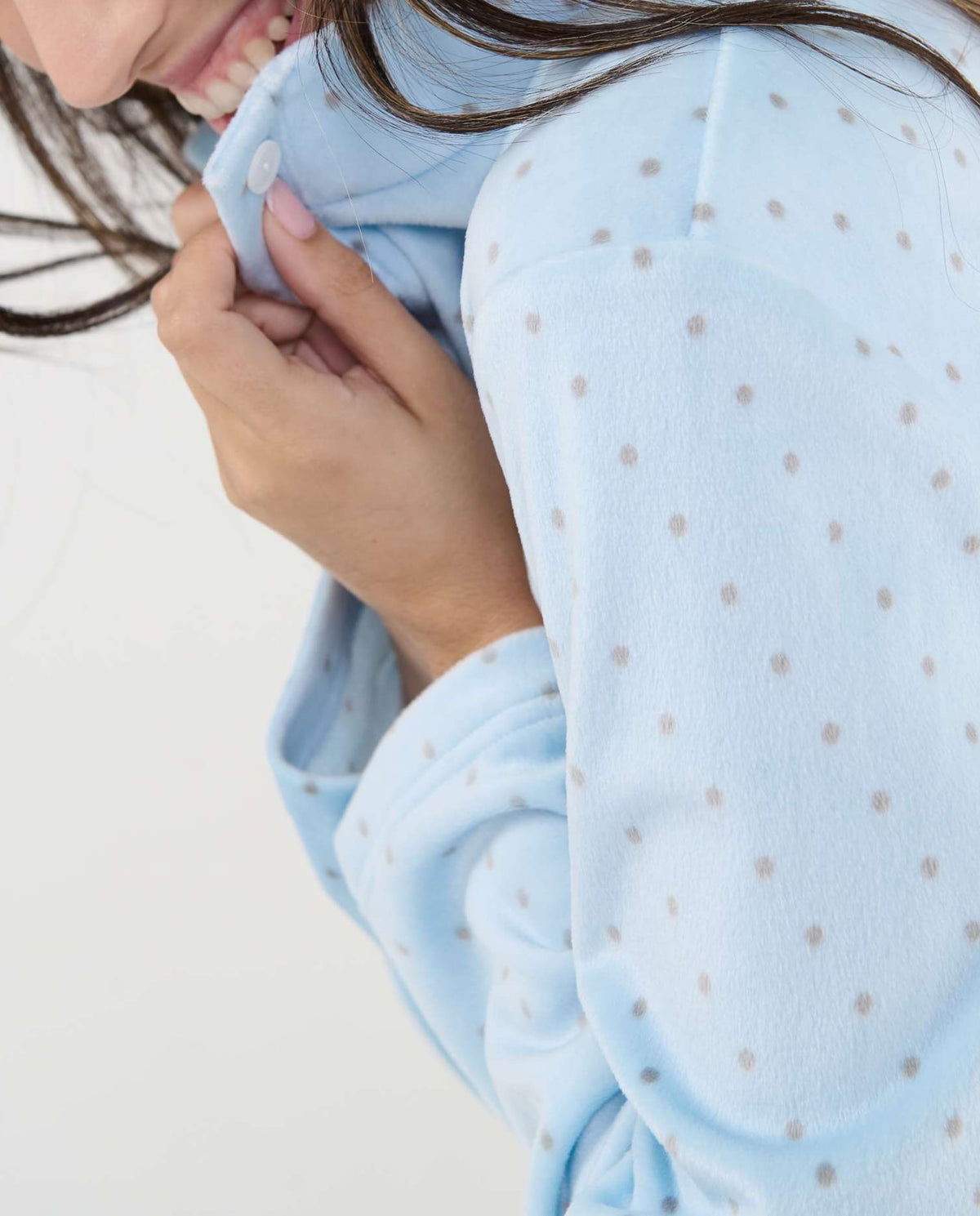 Mujer sonriente sujeta el cuello de una pijama polar celeste con lunares, ideal para estar cómoda y a la moda en casa.