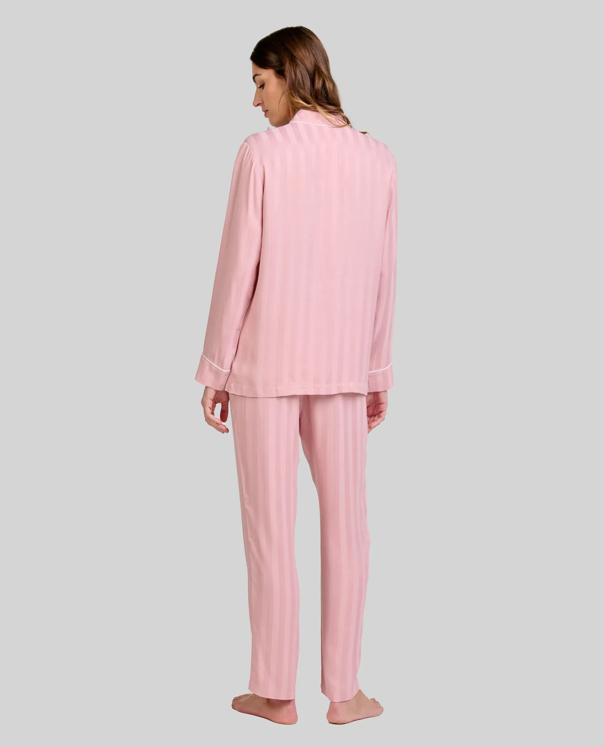 Mujer de espaldas luce pijama rosa palo con rayas verticales y manga larga con detalle vivo en puños