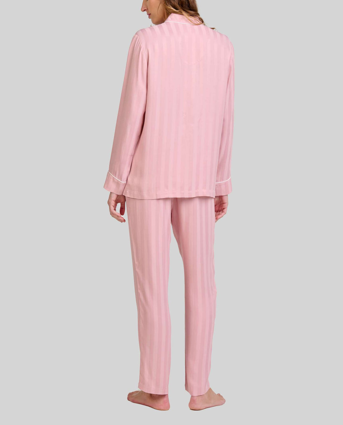 Mujer de espaldas luce pijama rosa palo con rayas verticales y manga larga con detalle vivo en puños