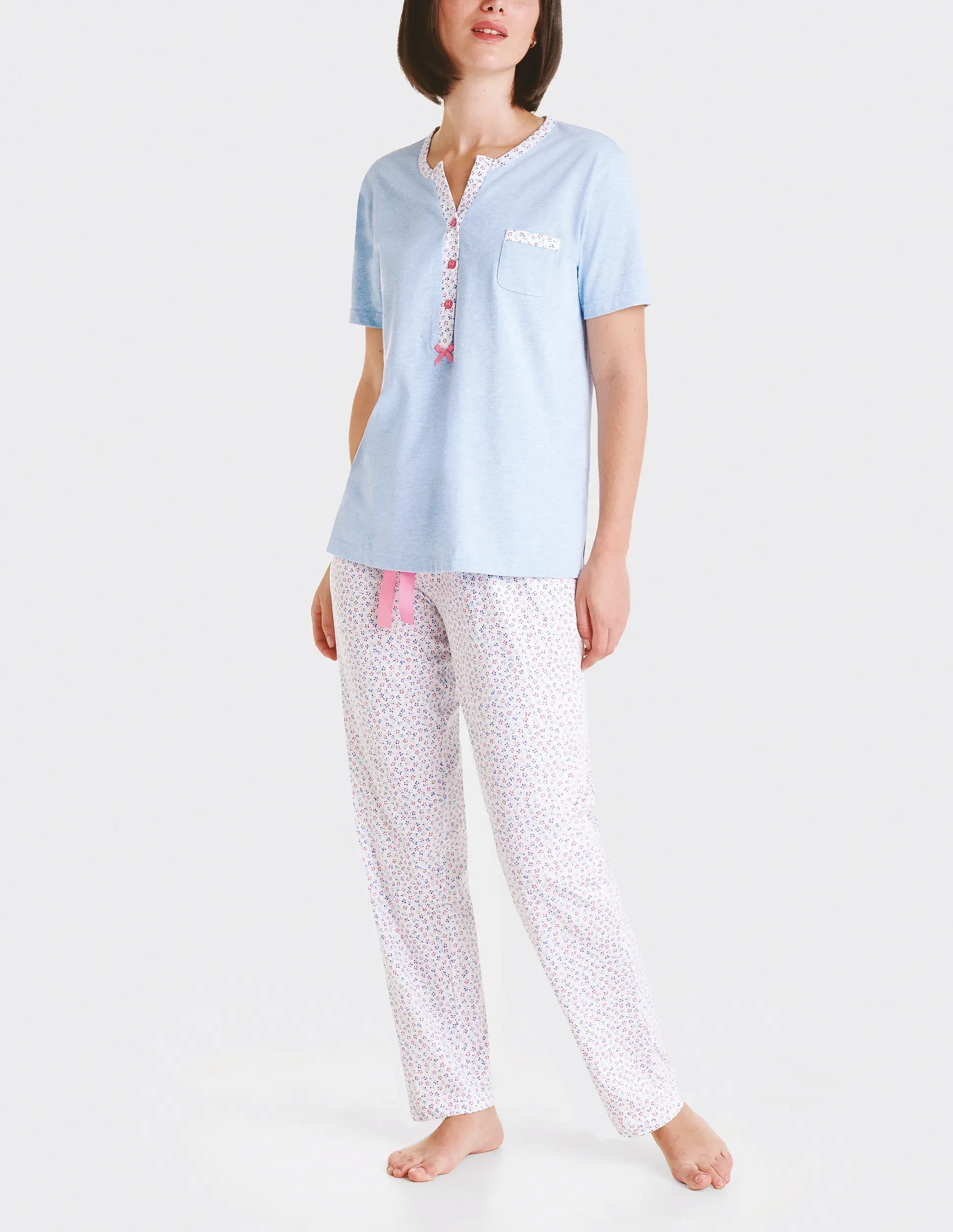 Mujer con camiseta de pijama azul claro de manga corta y pantalón de pijama de flores con lazo de raso rosa.