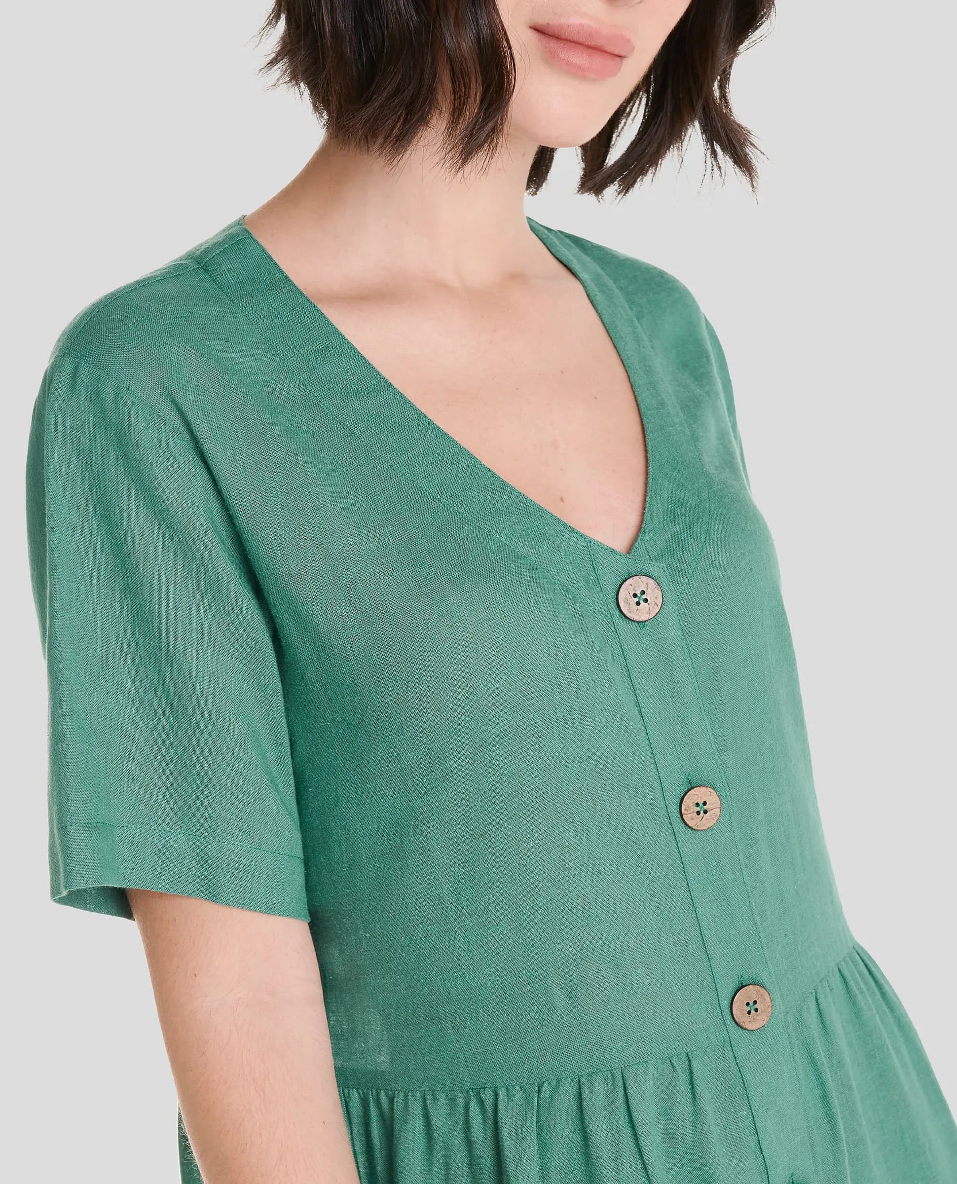 Detalle del escote en pico sin cuello, abotonado del vestido corto de lino verde de verano marca LOHE