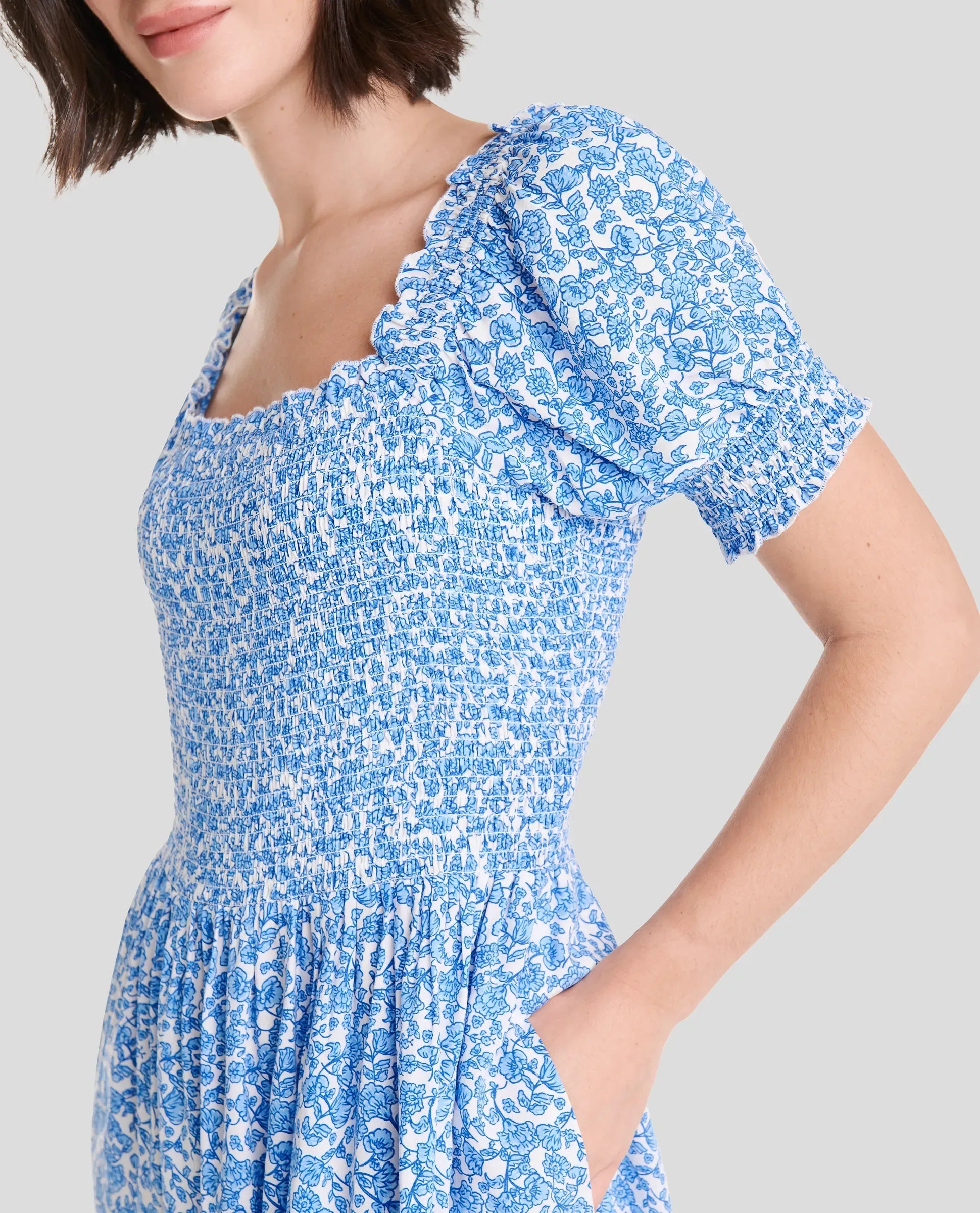 Mujer vistiendo un vestido corto floral azul y blanco con mangas abullonadas y un cintura fruncida