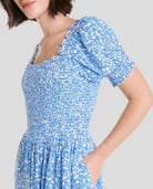 Mujer vistiendo un vestido corto floral azul y blanco con mangas abullonadas y un cintura fruncida