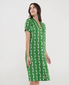Mujer con vestido playero verde de manga corta abotonado y patrón geométrico blanco.