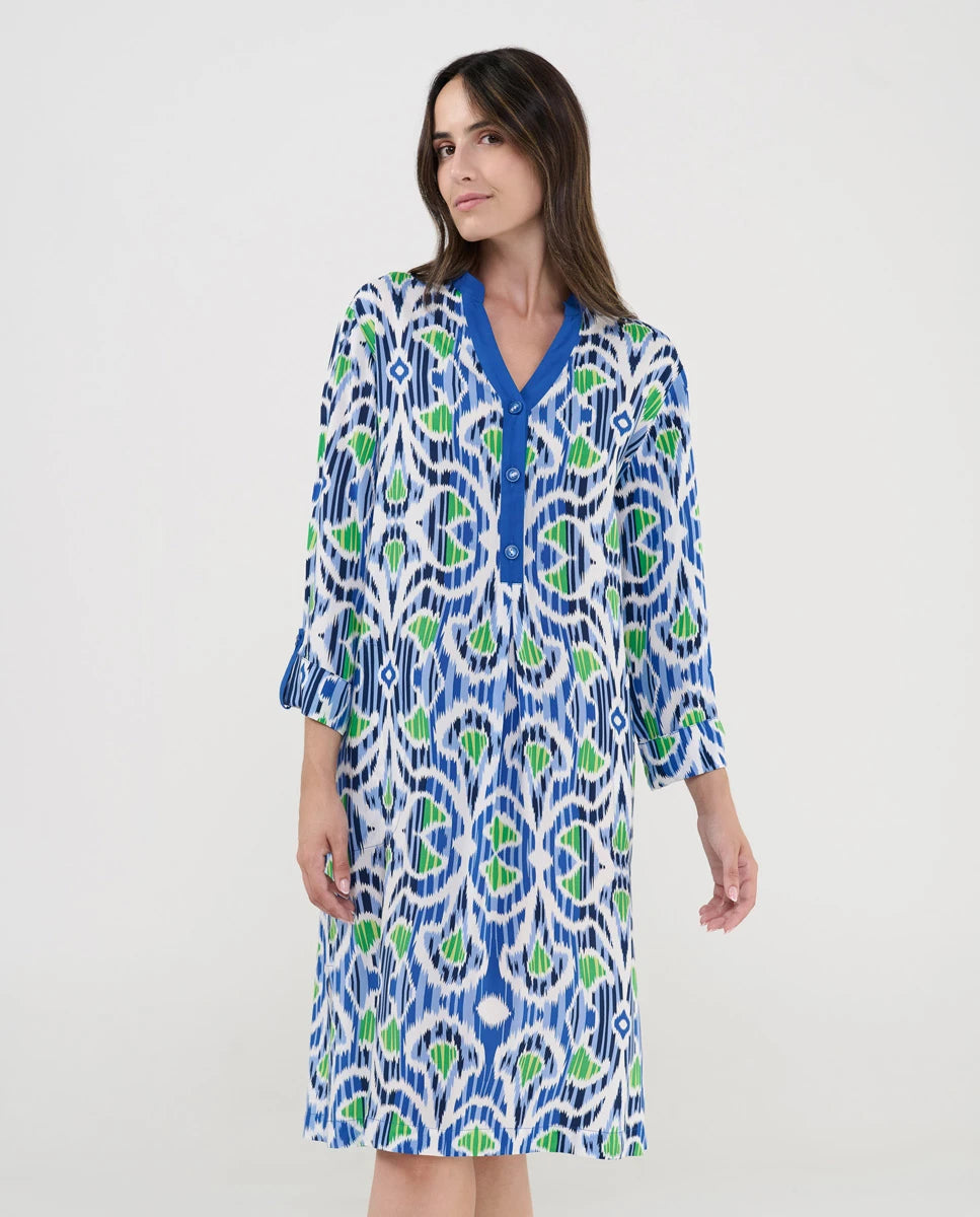 Mujer con vestido estampado azul y verde caminando junto a una piscina al aire libre.