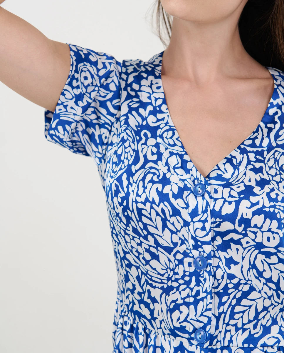 Detalle del torso de una mujer con vestido veraniego azul y blanco estampado, escote en V y botones frontales.