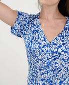 Detalle del torso de una mujer con vestido veraniego azul y blanco estampado, escote en V y botones frontales.