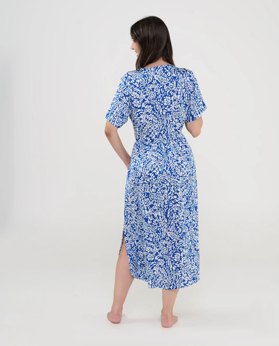 Vista trasera de una mujer con vestido midi azul estampado en blanco y abertura lateral.