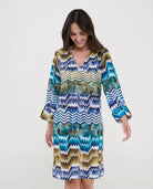 Mujer con vestido midi de estampado chevrón en tonos azul, turquesa y dorado con escote en V y mangas tres cuartos.