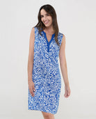 Mujer sonriente con vestido playero azul sin mangas y estampado blanco.