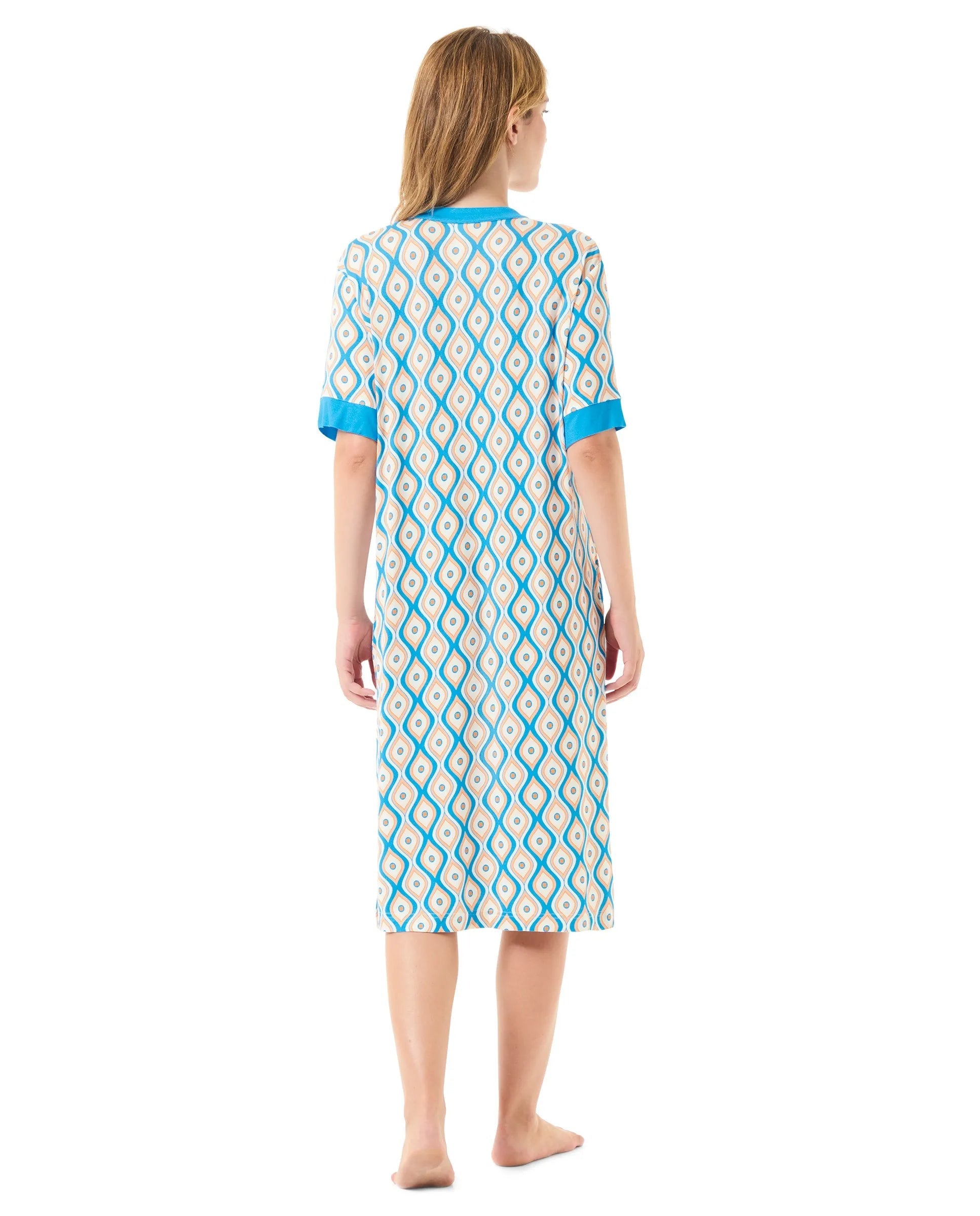 Una mujer descalza de espaldas luce un vestido de longitud media con estampado y detalles en azul en las mangas y el cuello.